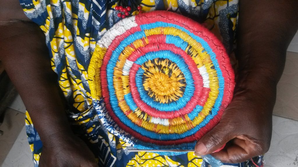 Aiguille à tricoter en main, Marie Mawabo confectionne un panier à base d’emballages plastiques recyclés