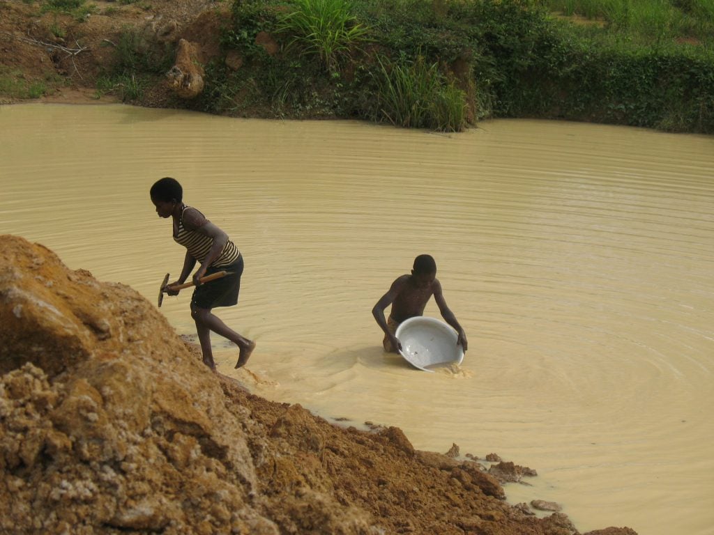  Les pieds noyés dans une fosse béante, deux enfants remuent l'eau boueuse à la recherche de l'or dans un chantier minier abandonné à l'Est Cameroun